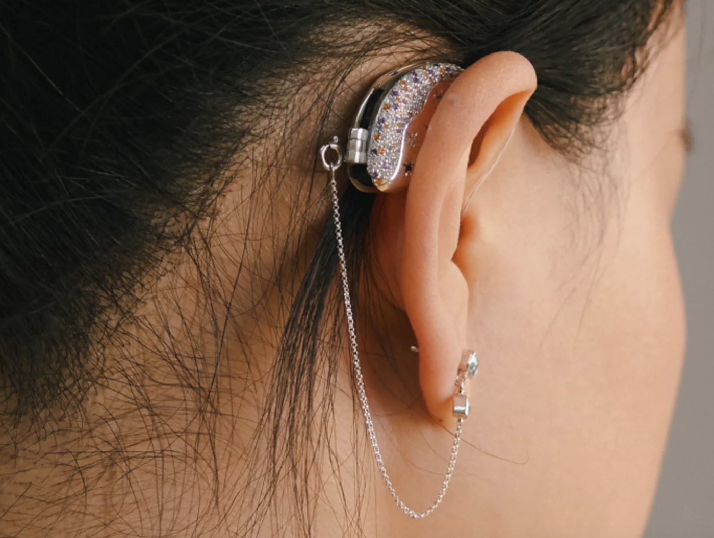 Close up photo shows Woman wears hearing aid cover in silver and diamanté